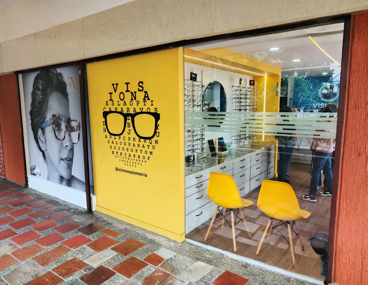 Fachada de vidrio de Óptica Visiona con su pared amarilla, sillas y vitrinas de monturas